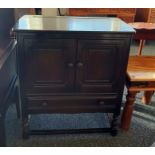 Dark elm Ercol dresser base with two cupboard doors above single drawer, turned and block supports