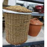 One wicker laundry basket containing a blue throw and large earthenware covered pot