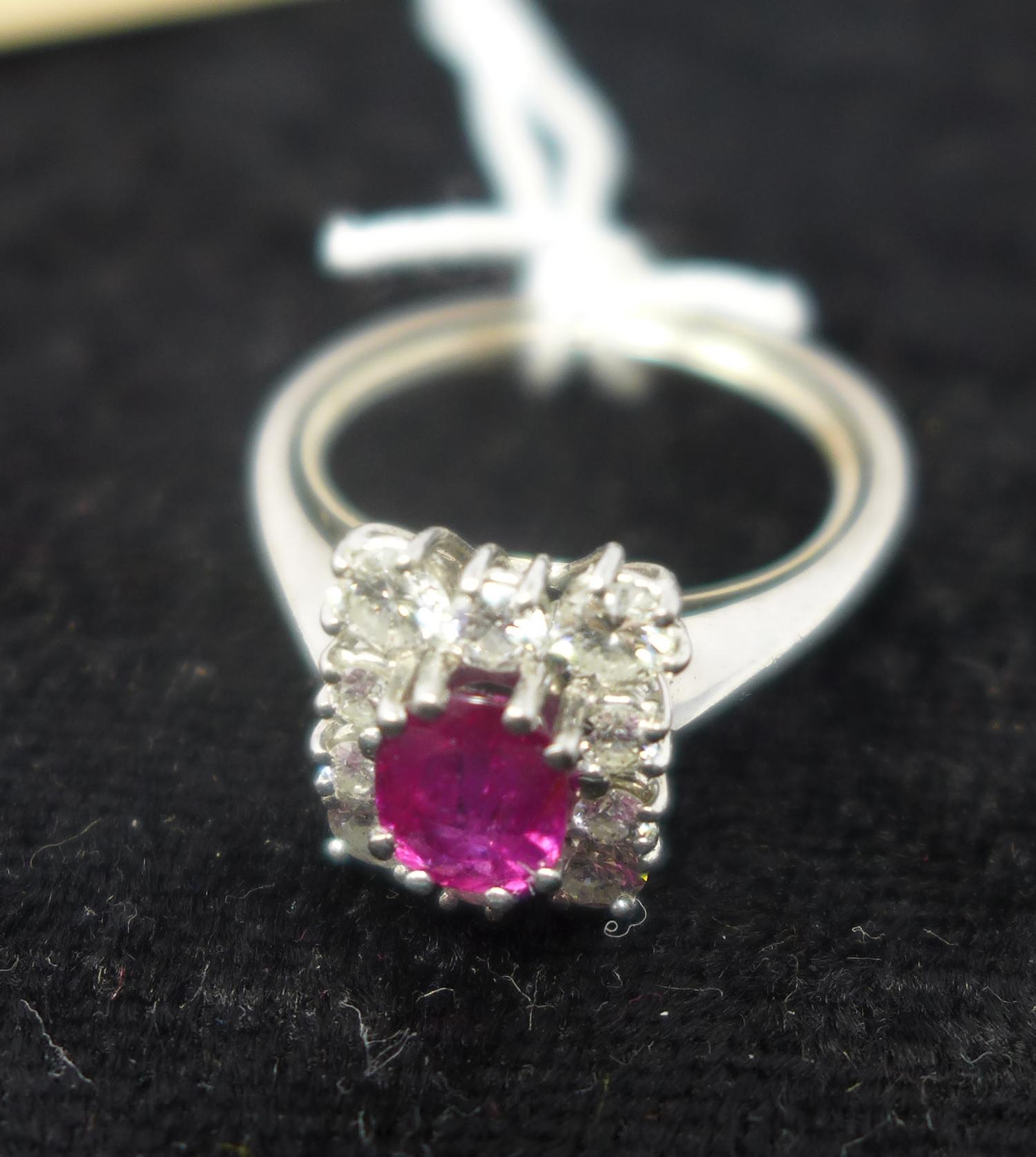 An 18ct white gold, natural ruby and diamond cluster ring, the central oval faceted ruby in a six-