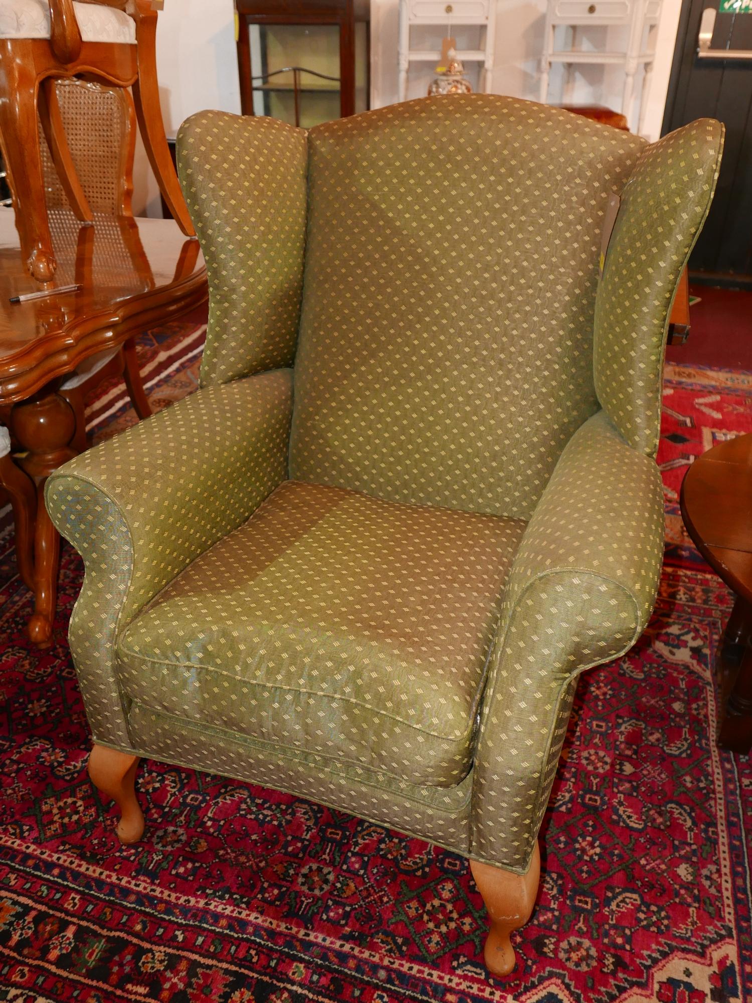 A contemporary wing back armchair in green and gold upholstery raised on beech wood legs