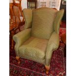 A contemporary wing back armchair in green and gold upholstery raised on beech wood legs