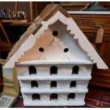 A white painted wooden birdhouse with slat roof, bearing plaque, H.85 W.80cm