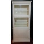 A contemporary white bookcase with two glazed doors, over cupboard door, raised on stepped base, H.