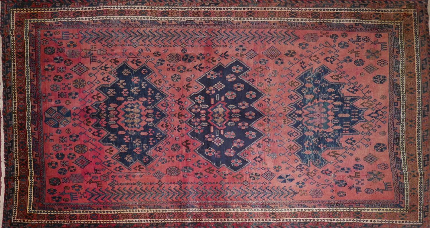 A North West Persian Kurdish carpet, triple eagle motifs on a pale rouge field, within stylised