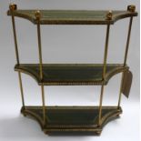 A gilt metal set of wall hanging shelves with gilt tooled green leather levels