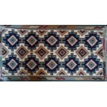 A Persian kelim woolen rug composed of a repeating geometric design in shades of blue, teal, maroon,