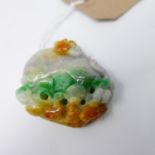 A large Chinese carved jade pendant adorned with a beast devouring a large fruit in veined hues of