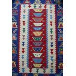 A multi coloured kelim rug with blue borders on red central panel L.168 W.110cm