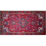 A Persian carpet with central geometric floral medallion surrounded by geometric motifs on a red