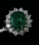 An 18ct white gold, emerald and diamond cluster ring, centrally set with a large, oval faceted