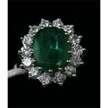 An 18ct white gold, emerald and diamond cluster ring, centrally set with a large, oval faceted