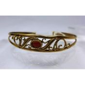 A 9ct yellow gold garnet bangle centrally set with a garnet cabochon flanked by floral arabesques,