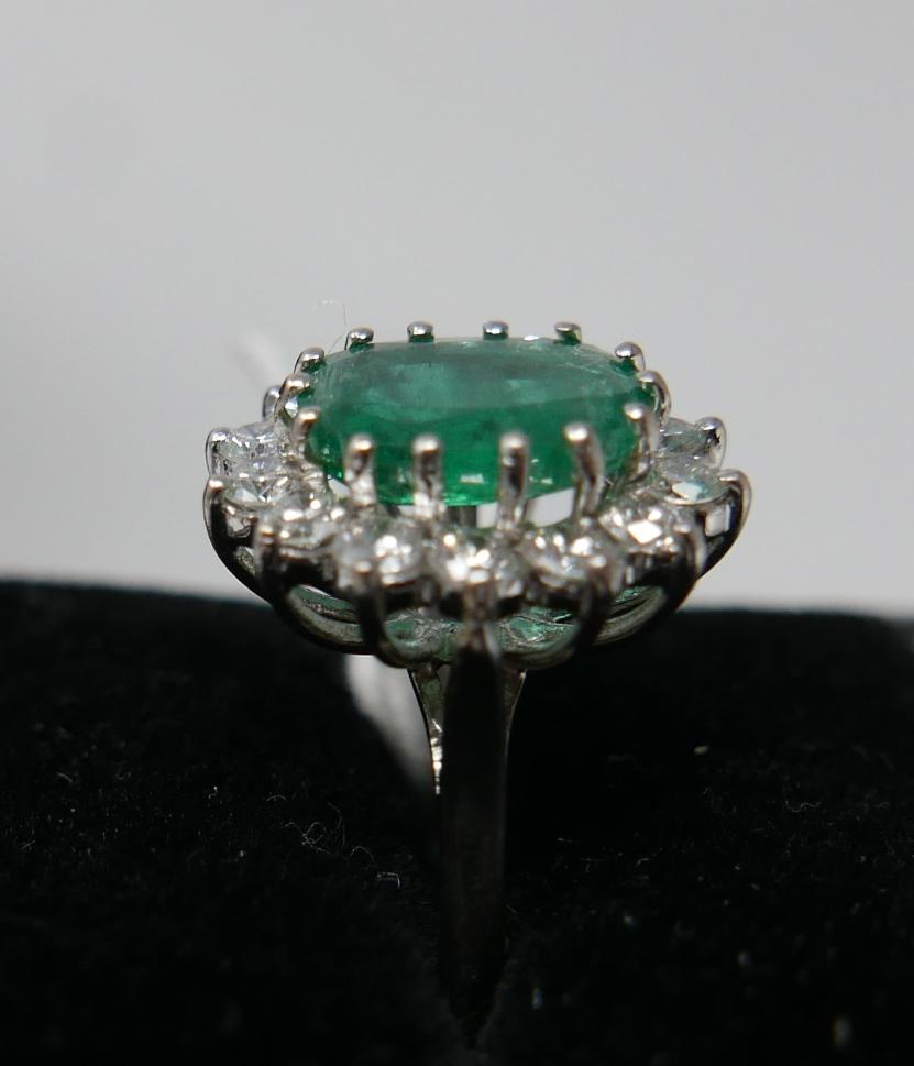 An 18ct white gold, emerald and diamond cluster ring, centrally set with a large, oval faceted - Image 6 of 6