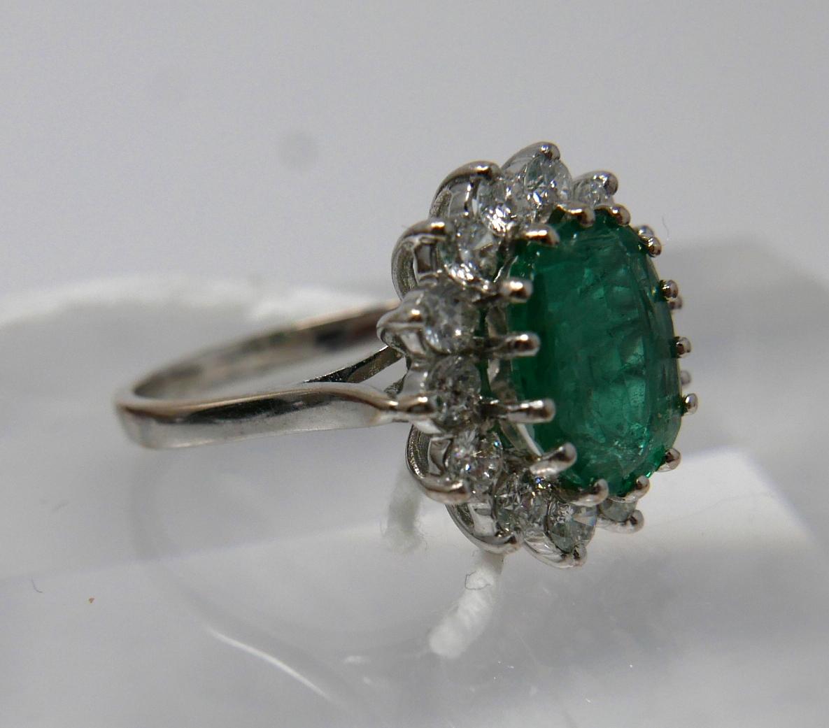 An 18ct white gold, emerald and diamond cluster ring, centrally set with a large, oval faceted - Image 2 of 6