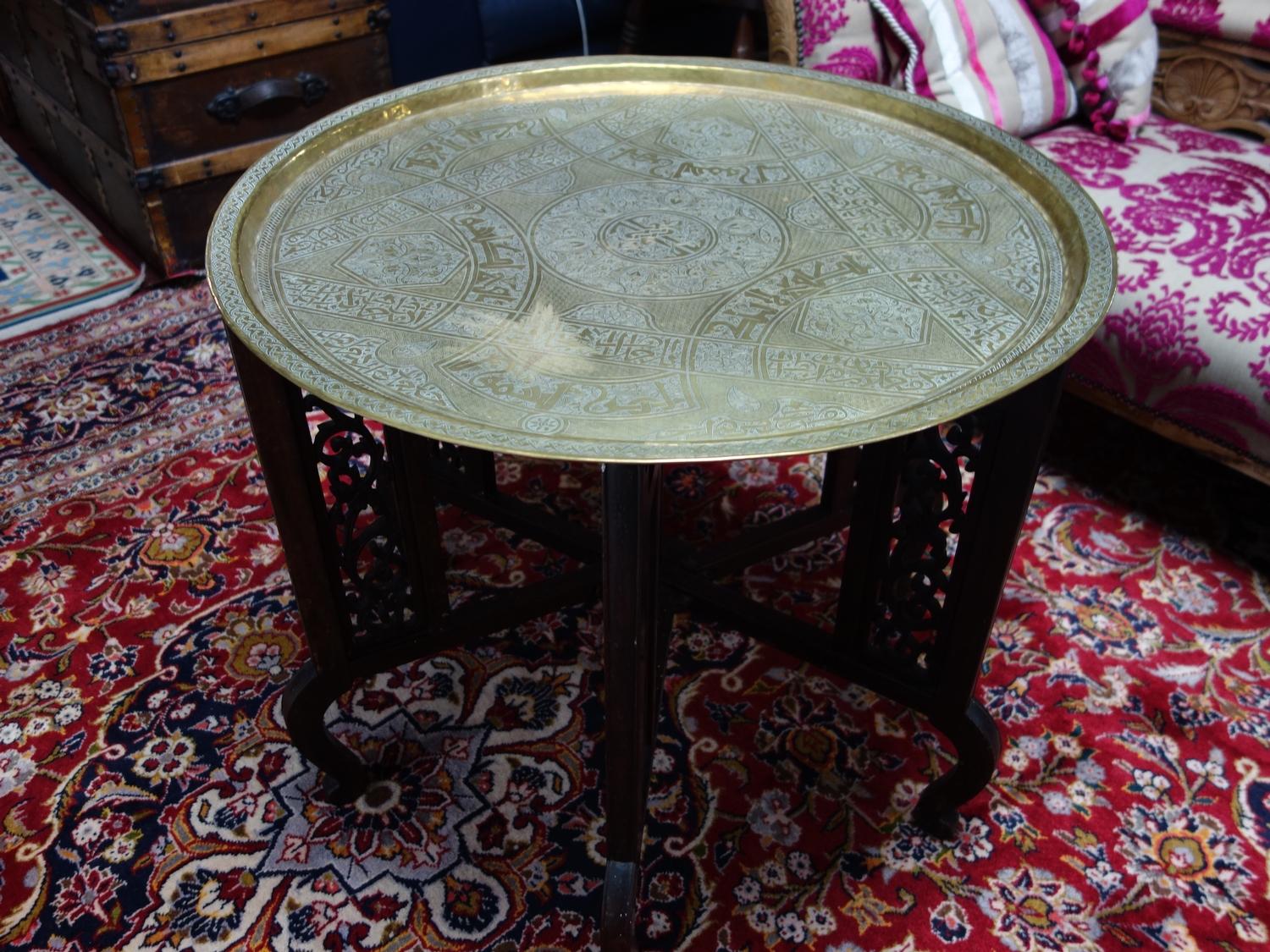 An Islamic brass tray on folding hardwood stand, the tray engraved with scrolling foliage, geometric