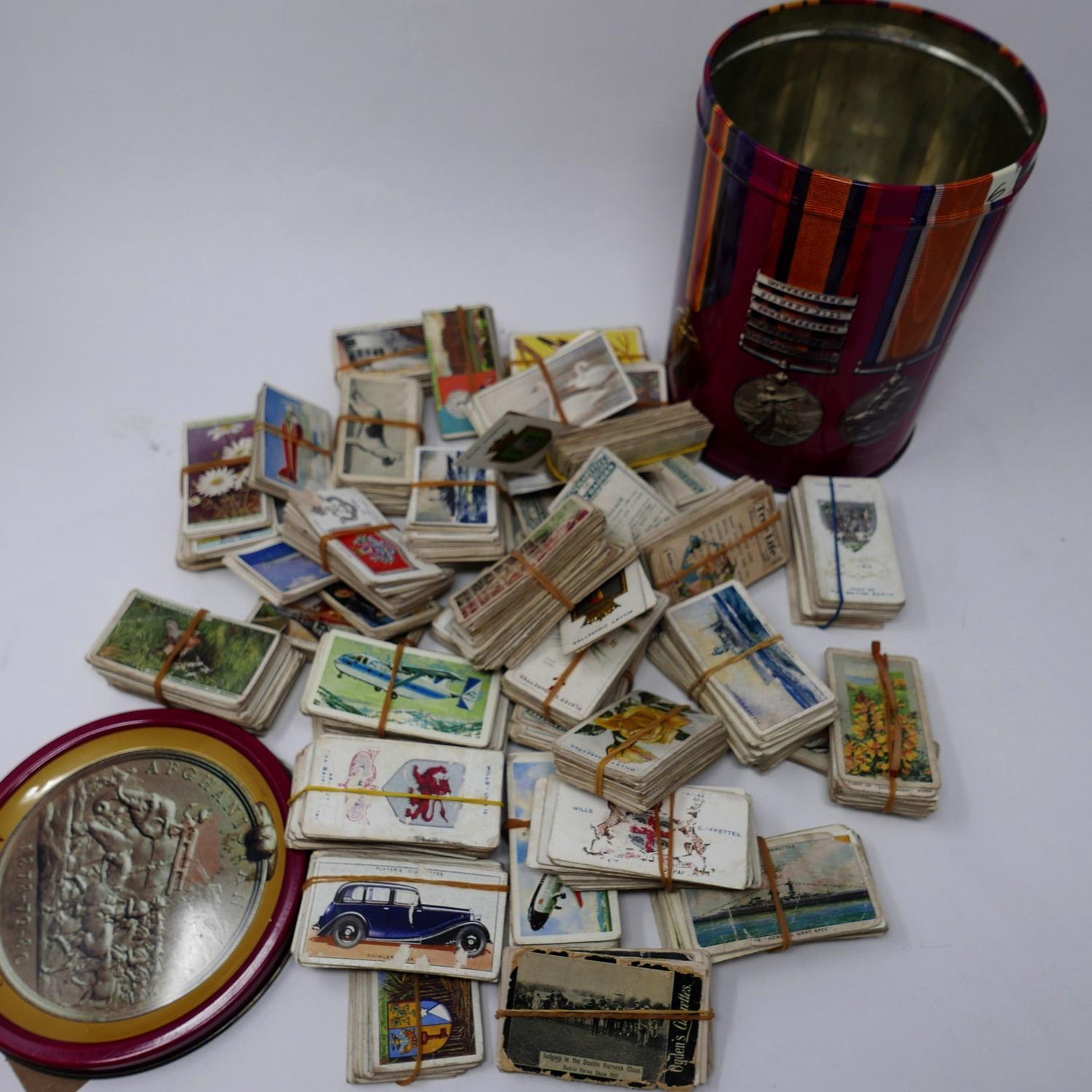 A collection of vintage cigarette cards in cylindrical tin