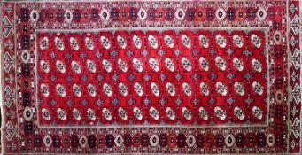 A North East Persian Turkoman carpet, repeating all over gul motifs on a rouge field within stylised