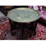 An Islamic brass tray on folding hardwood stand, the tray engraved with scrolling foliage, geometric