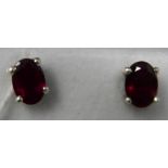 A boxed pair of sterling silver and ruby stud earrings, each earring composed of an oval, faceted