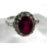 An 18ct white gold, ruby and diamond cluster ring, centrally set with an oval faceted ruby