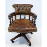 A mahogany captains swivel desk chair, with brown leather buttoned upholstery, raised on castors