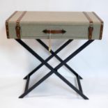 A campaign style console table, in the form of a bound trunk, raised on folding X frame base, H.81