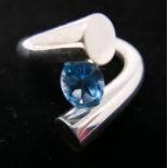 A sterling silver contemporary cross-over ring centrally set with a faceted oval blue topaz, Size: