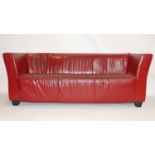 A red leather three seater sofa raised on block feet