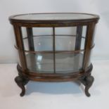 An early 20th century burr walnut oval display cabinet, raised on scrolling floral legs, H.78 W.85