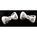 A boxed pair of white gold, bow-shaped stud earrings each set to the centre with a round,