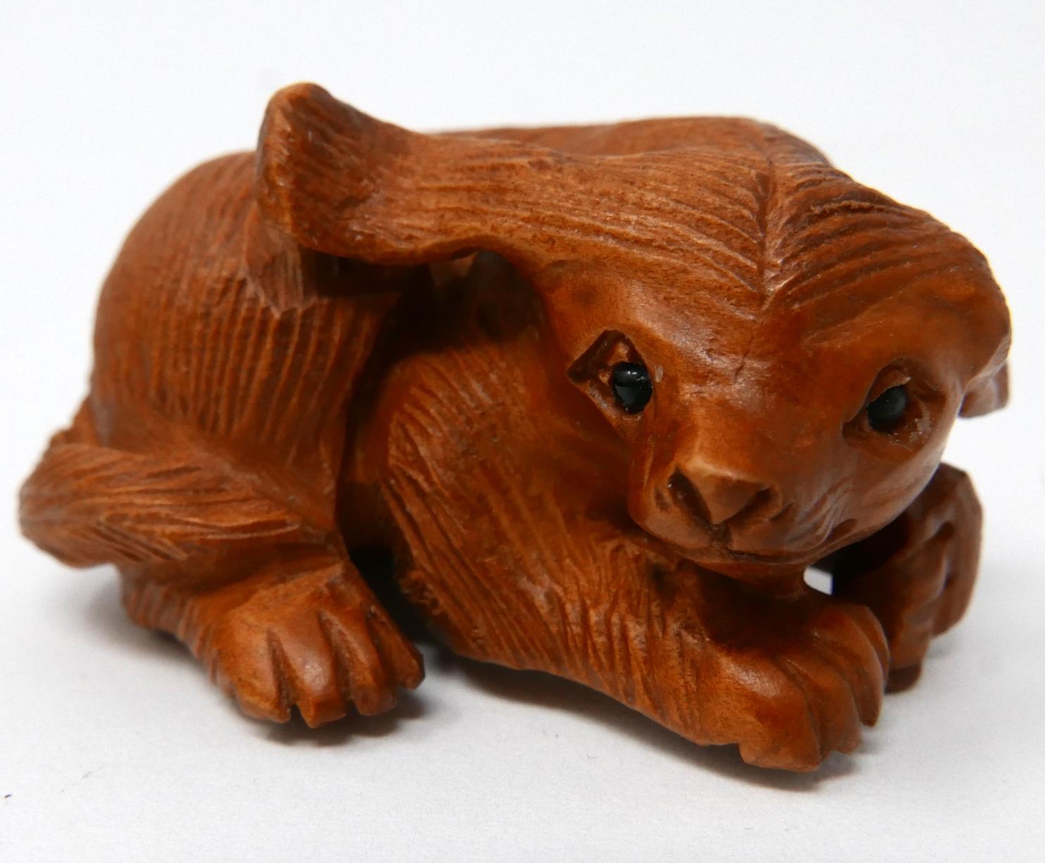 A Japanese carved wooden netsuke in the form of a seated dog