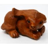 A Japanese carved wooden netsuke in the form of a seated dog