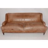 A Howard style stud bound tan leather sofa raised on turned legs