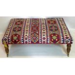 A large Kelim upholstered stool, raised on turned mahogany legs and castors, H.38 W.108 D.79cm