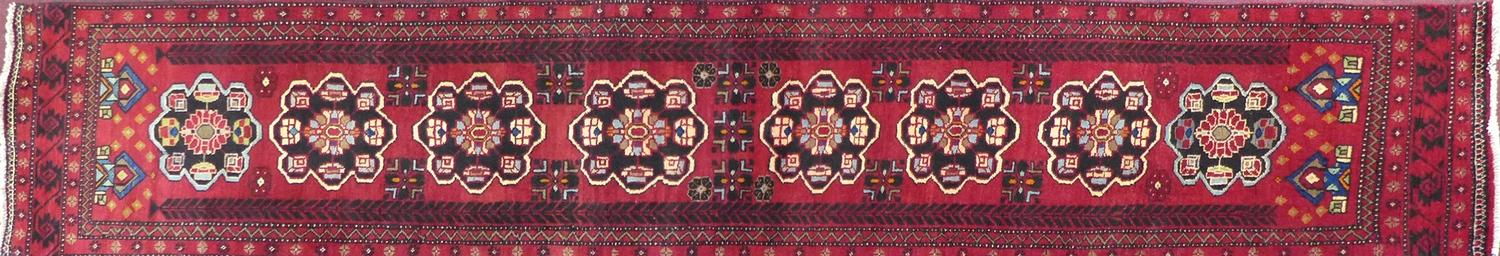 A North East Persian Kurdish runner, repeating pendent motifs with geometric motfis on a rouge