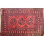 A 20th century Bokhara rug with triple gull motifs, on a red & black ground, contained by