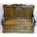 An early 20th century oak settle, with lion head arm rests and hinged seat, H.123 W.143 D.52cm