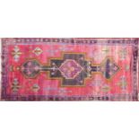 A Persian carpet with large geometric medallion, on a rouge ground, contained by geometric border,