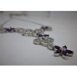 A sterling silver white sapphire and amethyst drop necklace of tendril form studded with flowers, L: