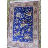An antique Persian Qum silk rug, signed, with hunting design on a blue ground, within floral border,