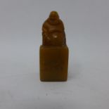 A Chinese, orange soapstone seal with a carved, smiling Buddha to top and character marks to front