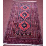 A Persian Balouch rug, red triple diamond medallions on a black ground, within geometric borders,