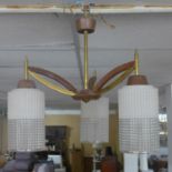 A set of three brass and teak ceiling lights with glass shades