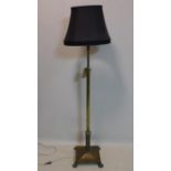 A brass standard lamp, raised on tapered support and four lion paw feet, with black shade, H.155cm