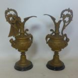 A pair of gilt metal ewers, with scrolling handles, having cherub and floral decoration, on circular