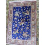 An antique Persian Qum silk rug, signed, with hunting design on a blue ground, within floral border,