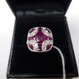 A boxed 18ct white gold Art Deco style, faceted ruby and brilliant-cut diamond ring to diamond-set