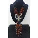 A substantial silver, amber and onyx tasselled necklace adorned with a large silver butterfly with