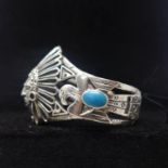 A sterling silver large bangle in the form of an American Indian with turquoise cabochon panels,