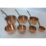 A vintage graduated set of 7 copper saucepans with iron handles